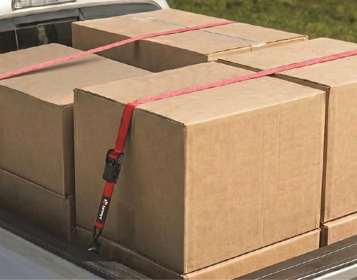 A red Tensys® ratchet strap, fastened to secure some cardboard boxes